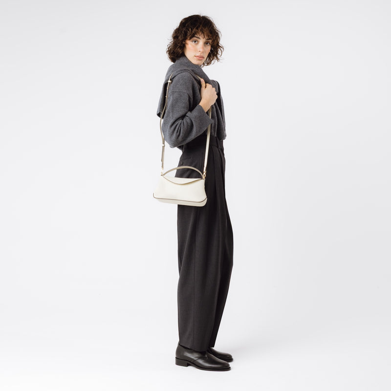 Model wearing STOW London's Mini East West in Spring Moon pebbled leather on her shoulder featuring gold-coated stainless steel hardware on a white background