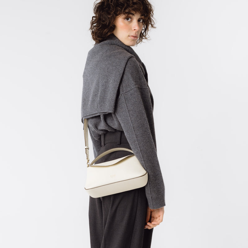 Model wearing STOW London's Mini East West in Spring Moon pebbled leather crossbody featuring gold-coated stainless steel hardware on a white background