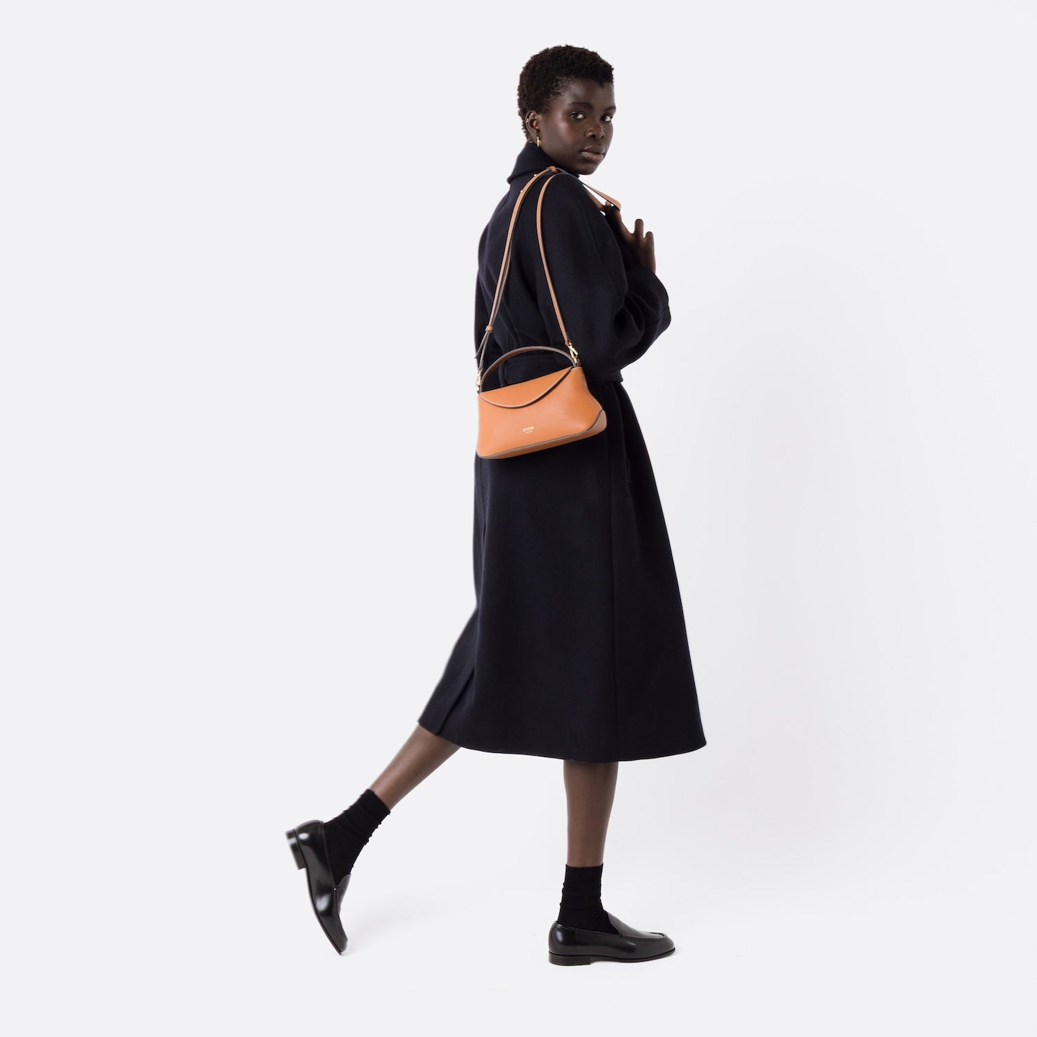 STOW London's Earth Tan Mini East West bag held by detachable strap over model's shoulder on a white background