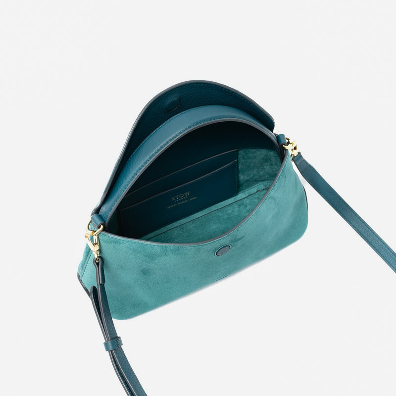 STOW London's Mini East West in Ocean Teal suede leather with flap open showing suede interior and slip pocket featuring gold-coated stainless steel hardware on a light grey background