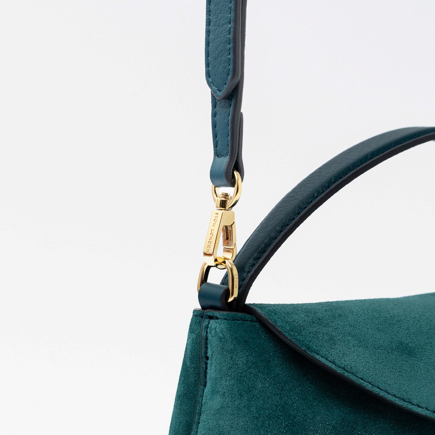 Close up of the detachable crossbody strap clip of STOW London's Mini East West in Ocean Teal suede leather featuring gold-coated stainless steel hardware on a light grey background