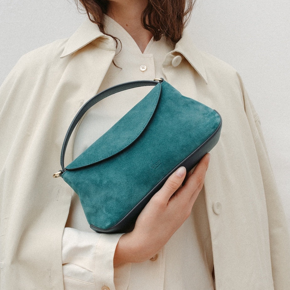 Model holding STOW London's Mini East West in Ocean Teal suede leather featuring gold-coated stainless steel hardware