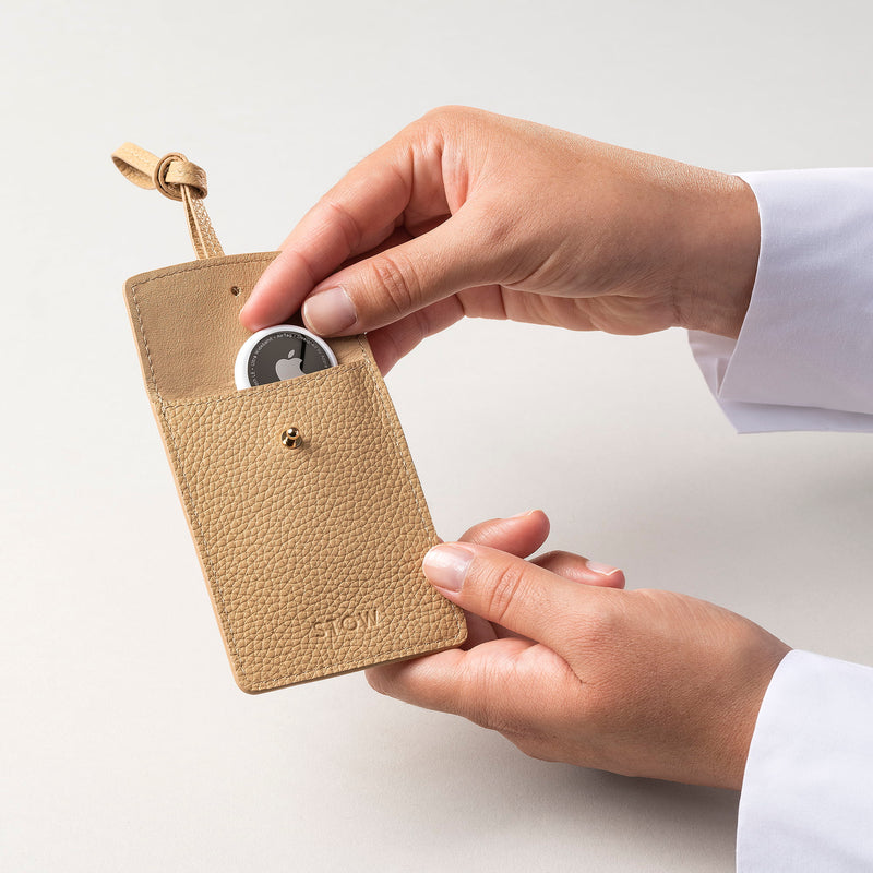STOW London Leather Multi Tag in Almond pebbled leather with model placing Apple AirTag inside.
