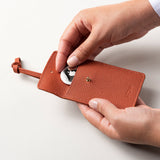 STOW Leather Multi Tag in Clay Orange pebbled leather with model placing Apple AirTag inside.