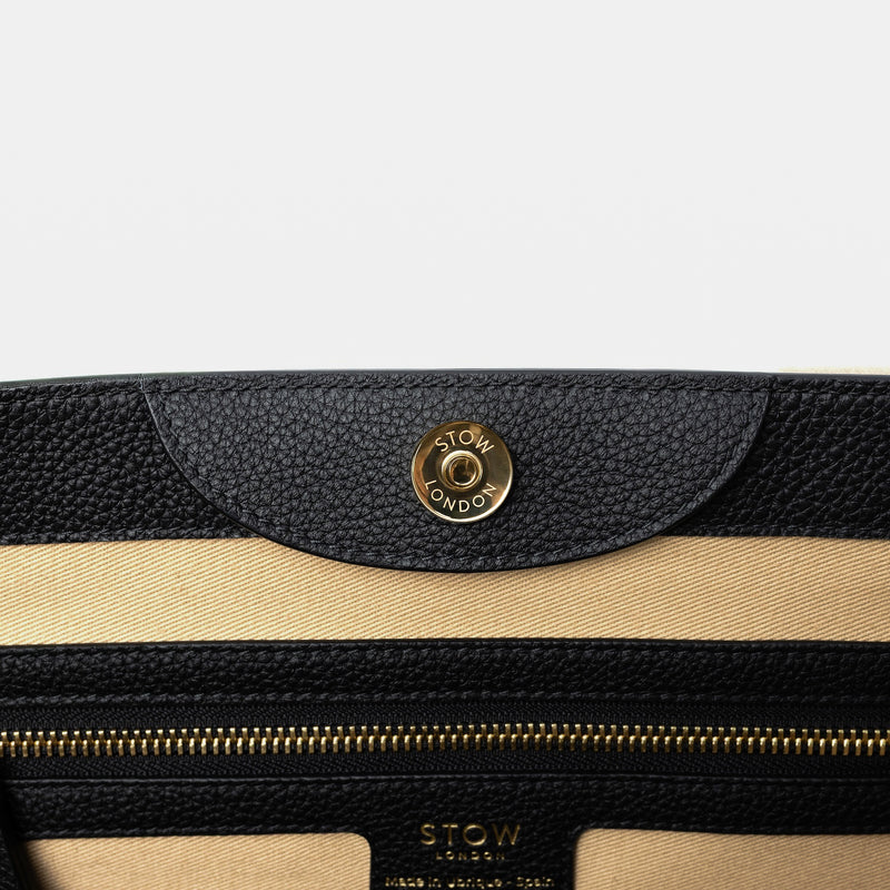 Close up of the magnet on STOW London's Nastro Tote bag in Black pebbled leather featuring a zip pocket on a light grey background