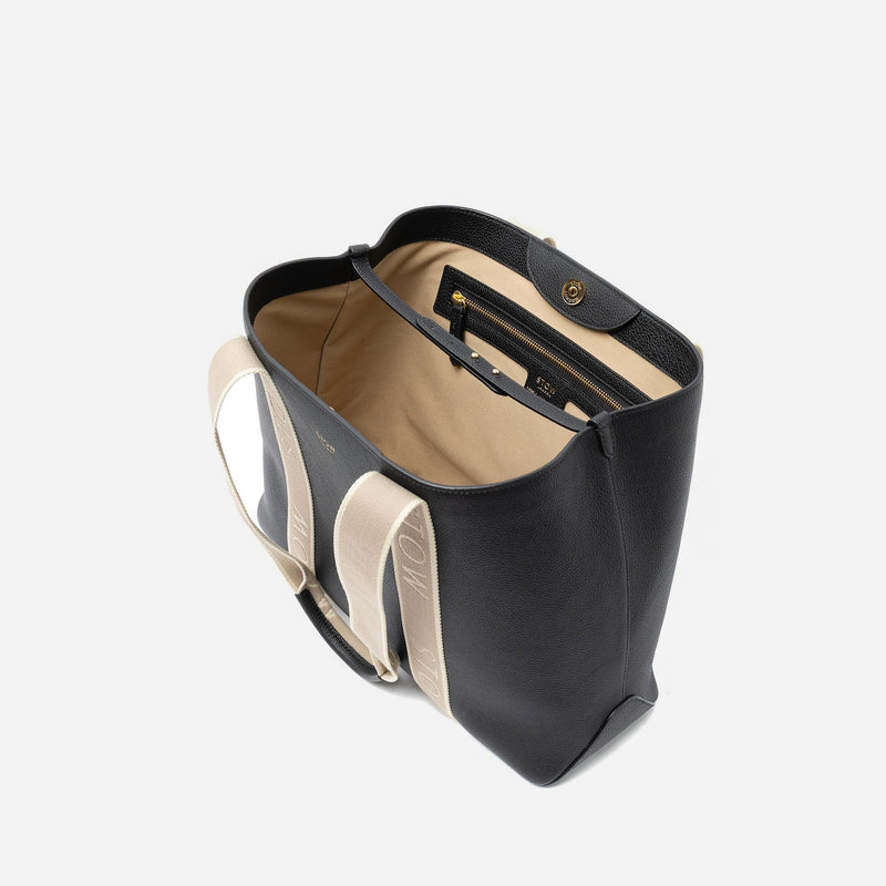 Top angled view of STOW London's Nastro Tote bag in Black pebbled leather with magnets open showing light beige cotton interior and zip pocket on a light grey background