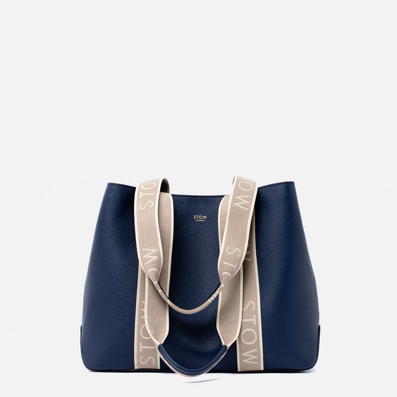 STOW London's Nastro Tote bag in Navy pebbled leather with beige nastro handles featuring 'STOW' branding on a light grey background