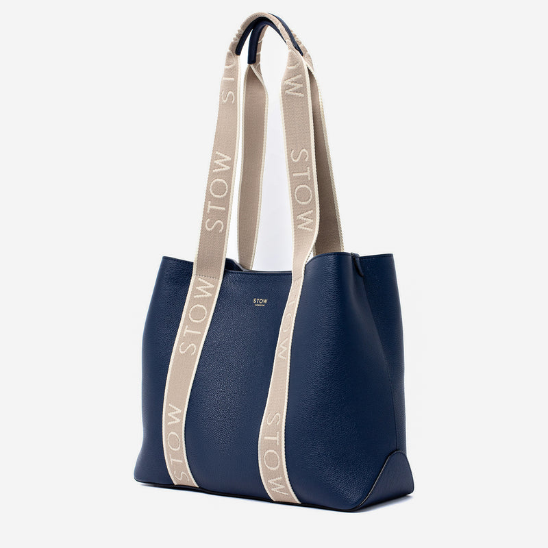 STOW London's Nastro Tote bag in Navy pebbled leather with beige nastro handles featuring 'STOW' branding on a light grey background