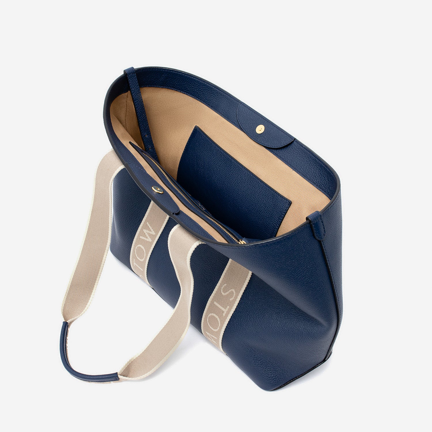 STOW London's Nastro Tote bag in Navy pebbled leather with magnets open showing cotton interior lining and slip pocket on a light grey background