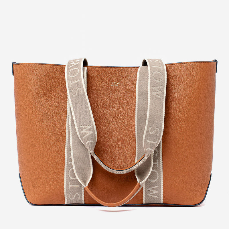 STOW London's Nastro Tote bag in Earth Tan pebbled leather with beige nastro handles featuring 'STOW' branding on a light grey background