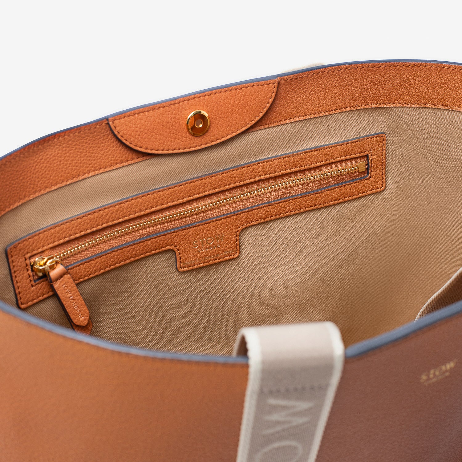 Close up of interior of STOW London's Nastro Tote bag in Earth Tan pebbled leather featuring magnet and zip pocket on a light grey background