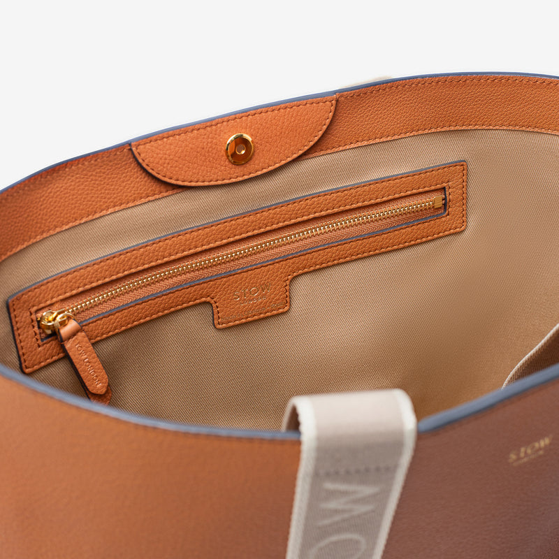 Close up of interior of STOW London's Nastro Tote bag in Earth Tan pebbled leather featuring magnet and zip pocket on a light grey background