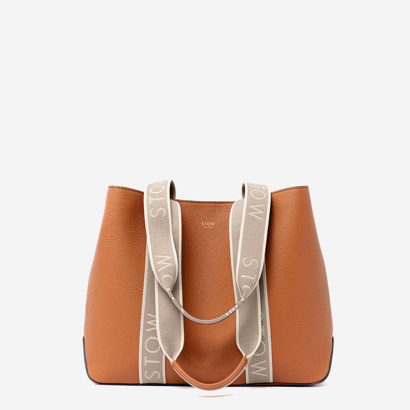 STOW London's Nastro Tote bag in Earth Tan pebbled leather with beige nastro handles featuring 'STOW' branding on a light grey background