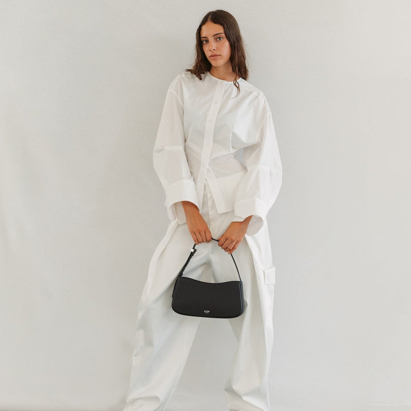 Model holding STOW London's Post Shoulder bag in Black smooth leather at her front featuring silver hardware