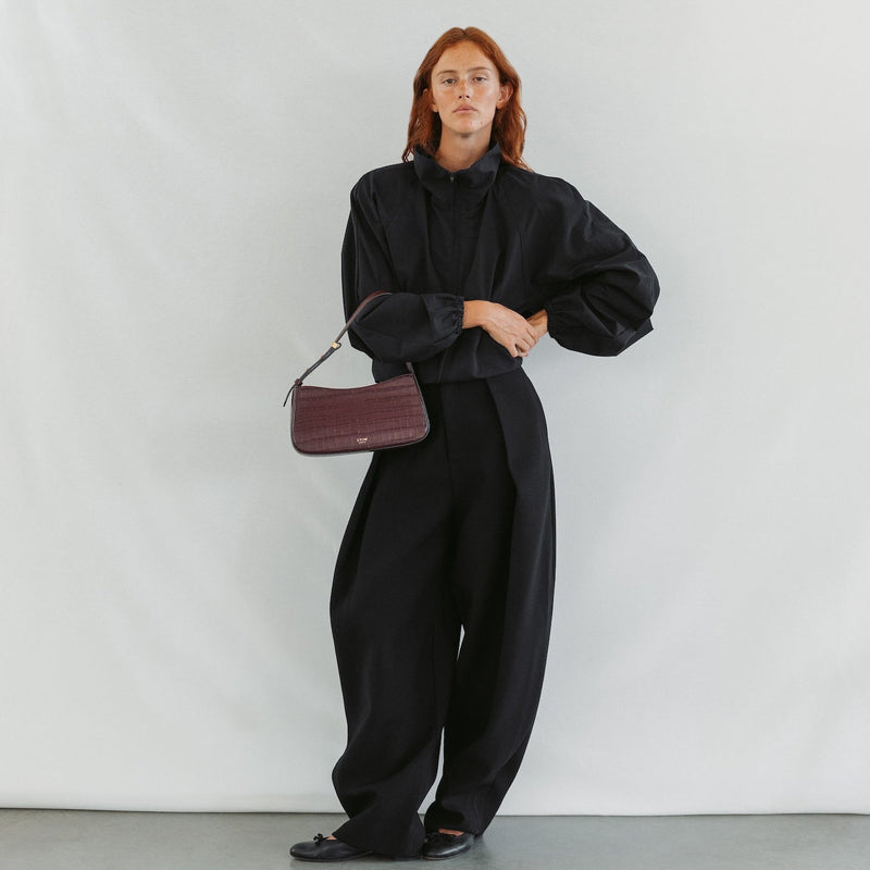 Model holding STOW London's Post Shoulder bag in Burgundy Embossed Croc leather featuring gold-coated stainless steel hardware 