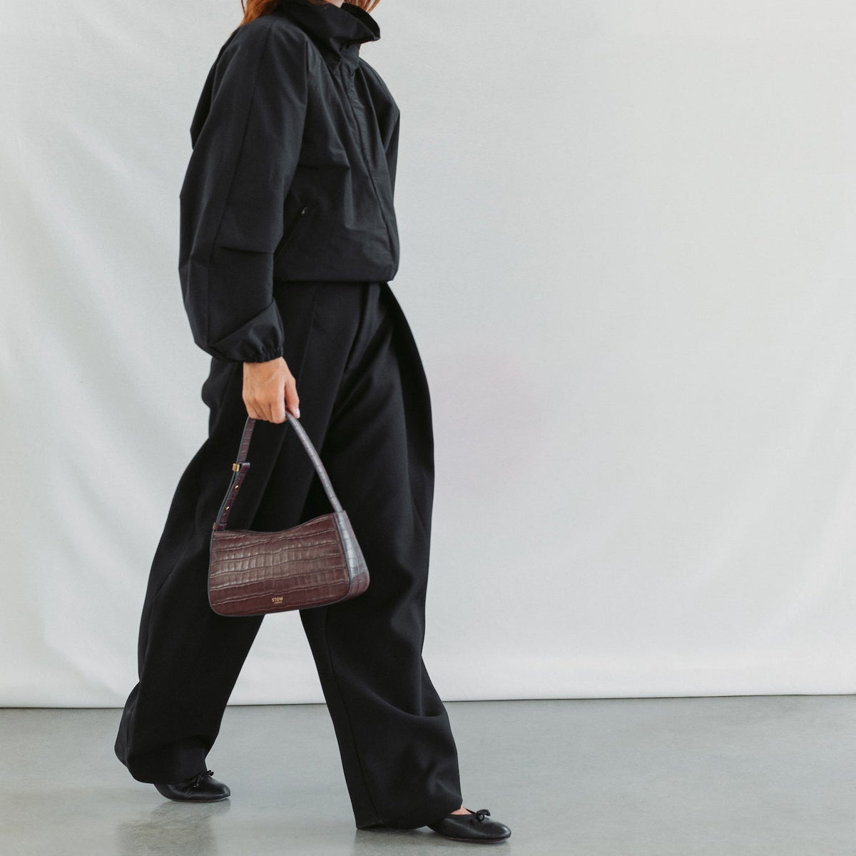 Model walking with STOW London's Post Shoulder bag in Burgundy Embossed Croc leather featuring gold-coated stainless steel hardware 