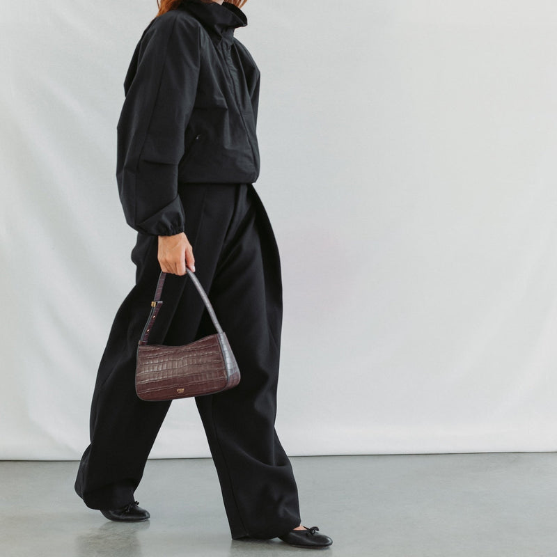 Model walking with STOW London's Post Shoulder bag in Burgundy Embossed Croc leather featuring gold-coated stainless steel hardware 