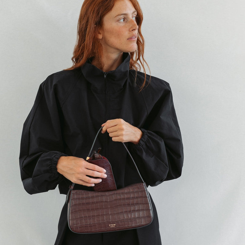 Model with STOW London's Post Shoulder bag and Glasses Case in Burgundy Embossed Croc leather featuring gold-coated stainless steel hardware 
