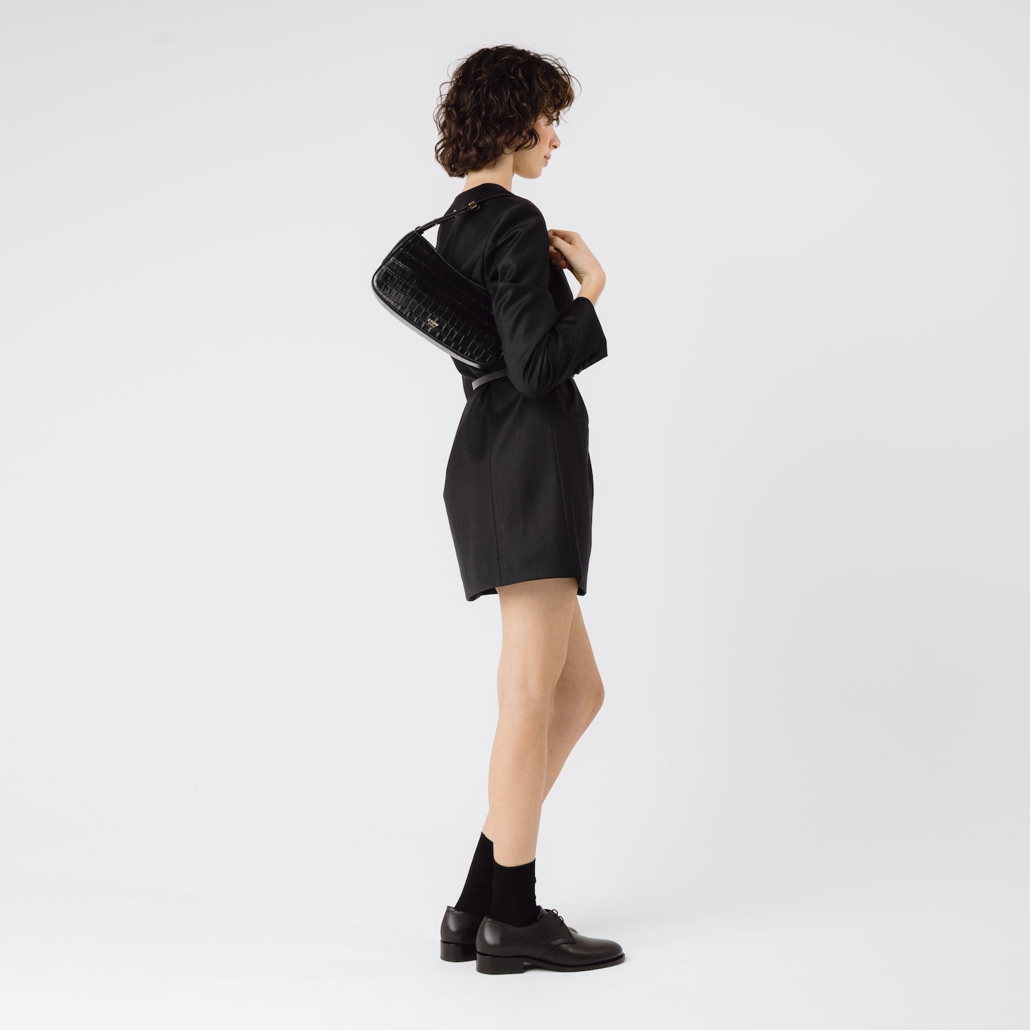Model wearing STOW London's Post Shoulder bag in Black Embossed Croc leather on her shoulder featuring gold-coated stainless steel hardware on a white background