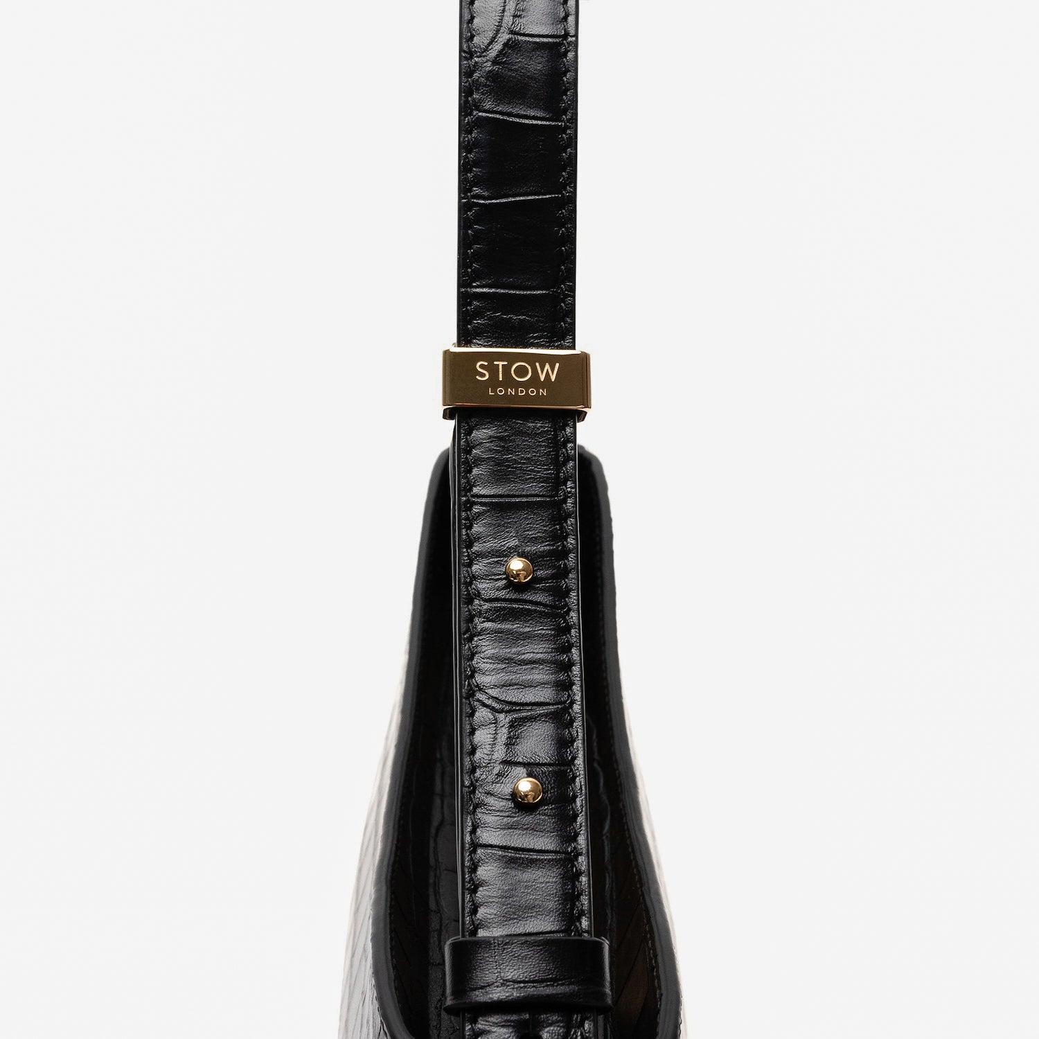 Close up of the gold hardware on the adjustable strap on Stow London's Post Shoulder in Black Embossed Croc leather on a light grey background