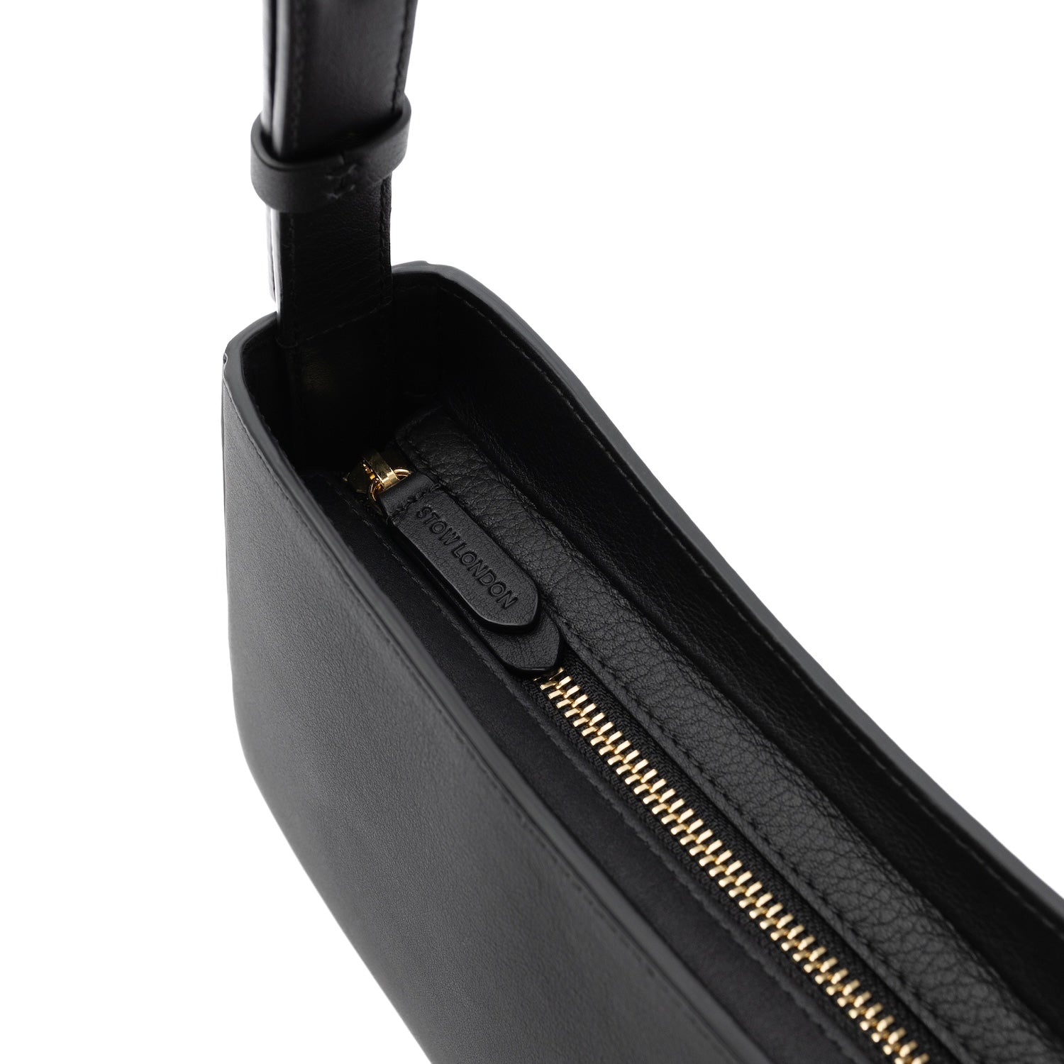 Close up of the zip top closure of STOW London's Post Shoulder bag in Black smooth leather featuring gold-coated stainless steel hardware and brand engraving on the pull tab on a white background