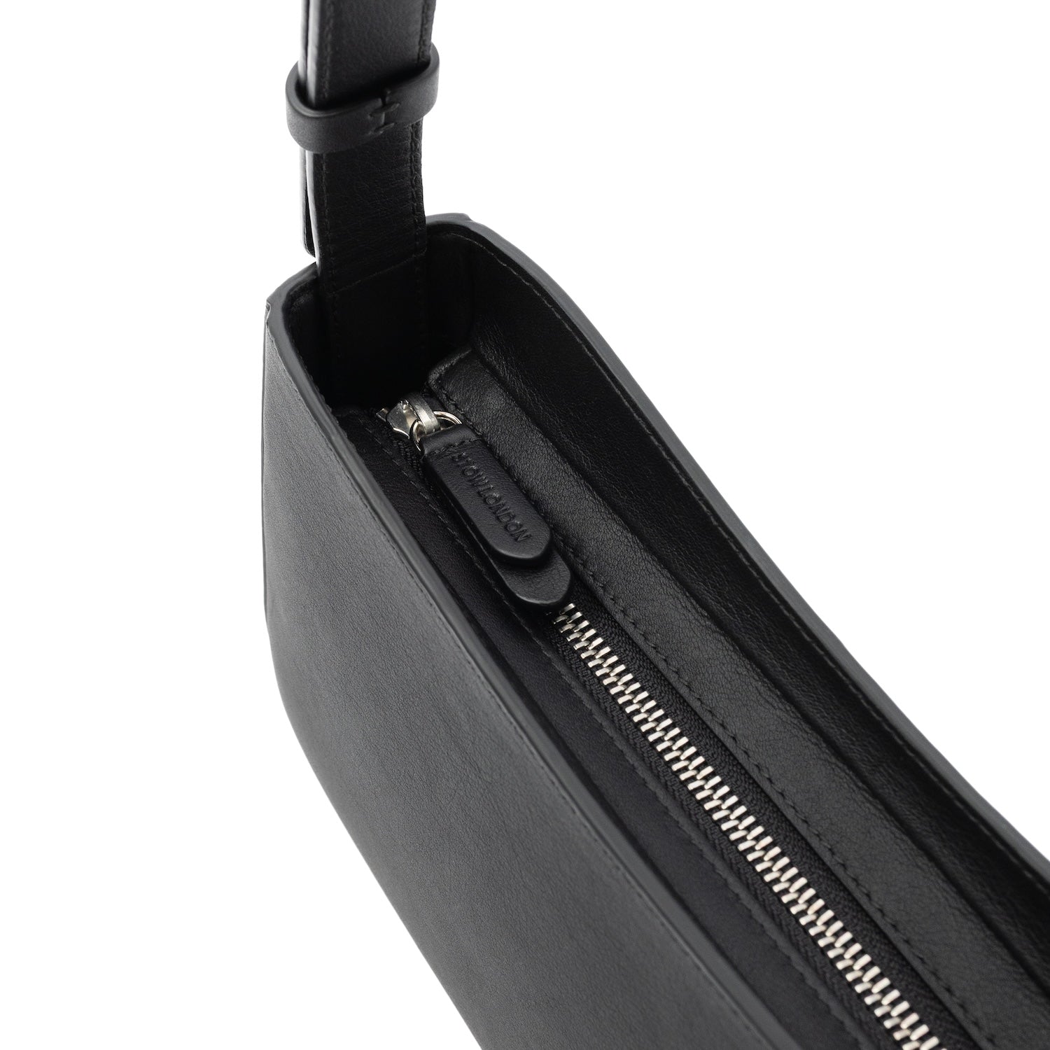 Close up of STOW London's zip closure on the Post Shoulder bag in Black smooth leather featuring silver hardware and brand engraving on the pull tab on a white background