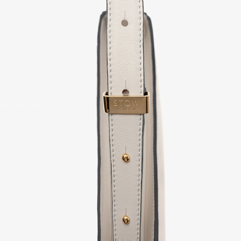 Close up of the gold hardware on the adjustable strap on Stow London's Post Shoulder in Cloud Grey smooth leather on a light grey background