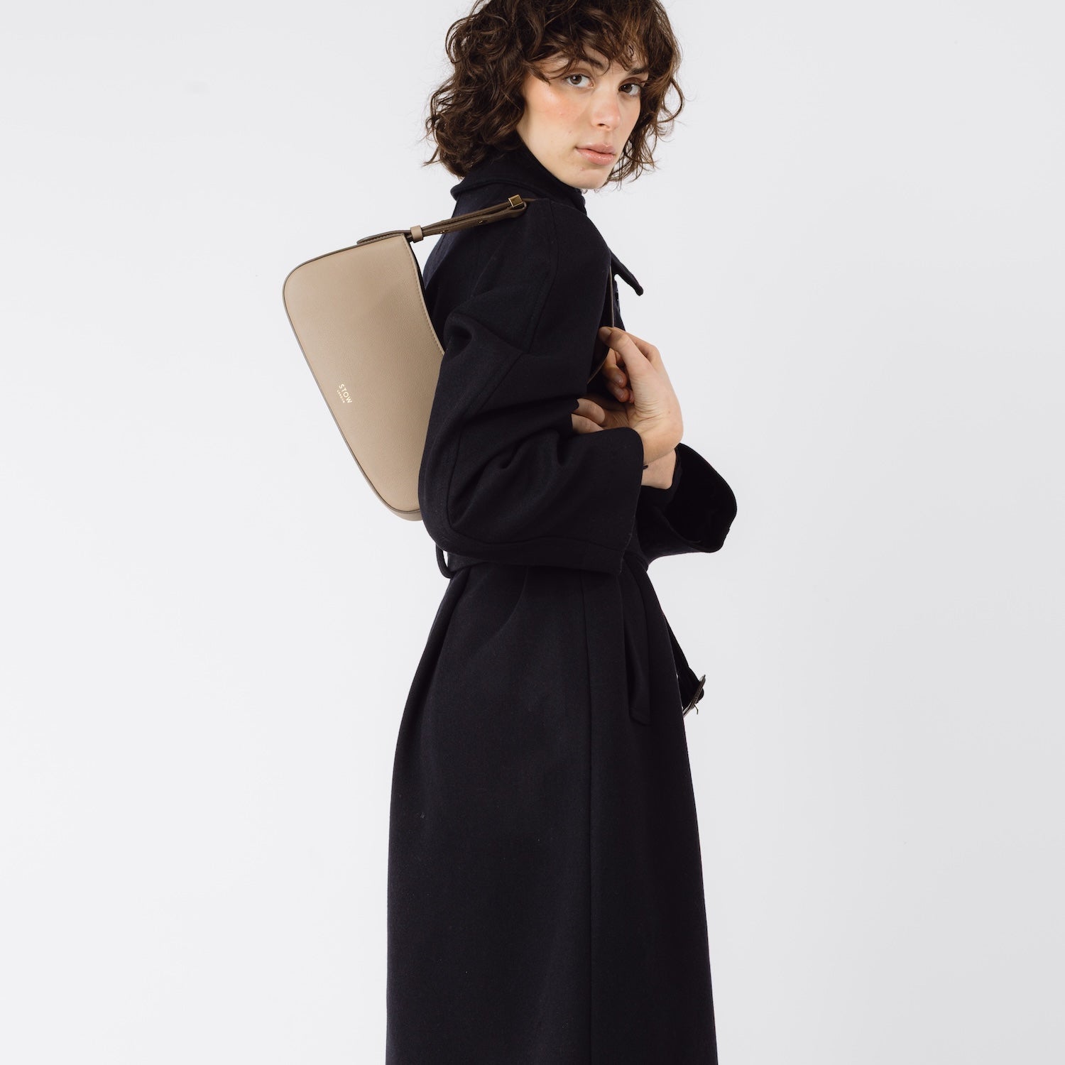 Model wearing STOW London's Post Shoulder bag in Warm Taupe smooth leather on her shoulder featuring gold-coated stainless steel hardware on a white background