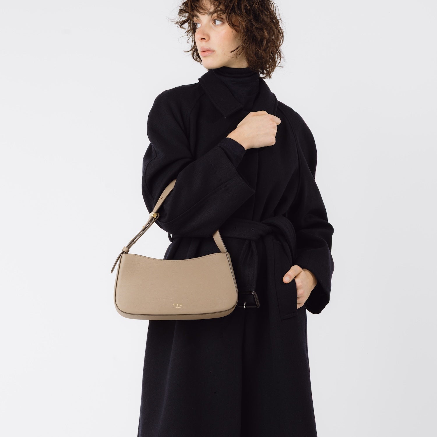 Model wearing STOW London's Post Shoulder bag in Warm Taupe smooth leather on her arm featuring gold-coated stainless steel hardware on a white background