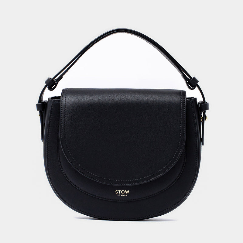 STOW London's Saddle bag in Black smooth leather with its short top handle on a light grey background