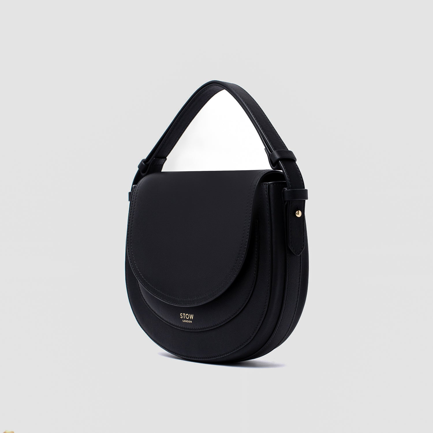 STOW London's Saddle bag in Black smooth leather with its short top handle on a light grey background