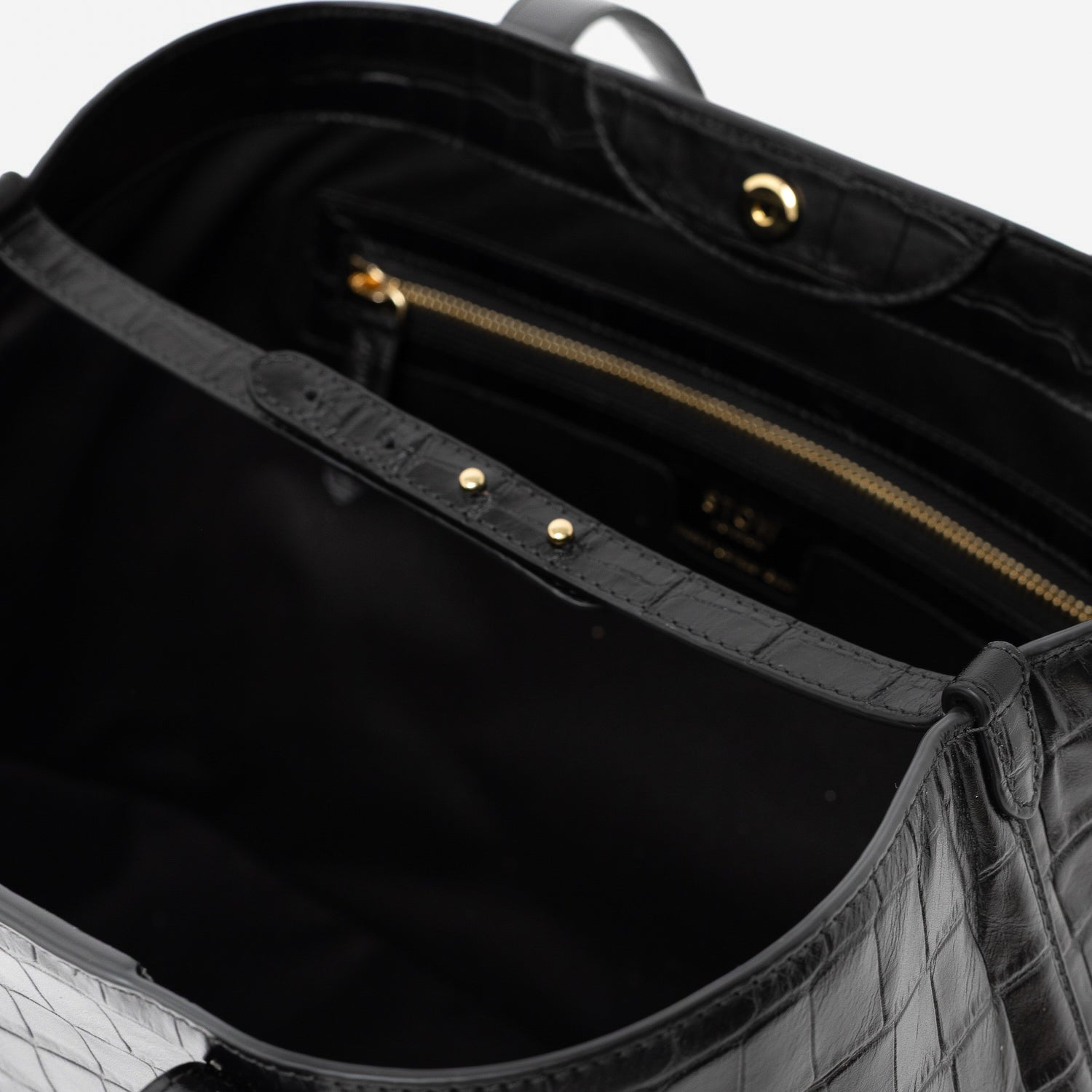 Close up of interior leather strap of Stow London's Everyday Tote Bag in Black Embossed Croc leather on a light grey background featuring zip pocket, magnetic closure and gold stainless steel hardware