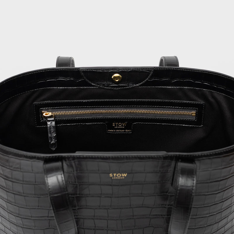 Close up of Stow London's Everyday Tote Bag in Black Embossed Croc leather on a light grey background featuring zip pocket, magnetic closure and gold hardware