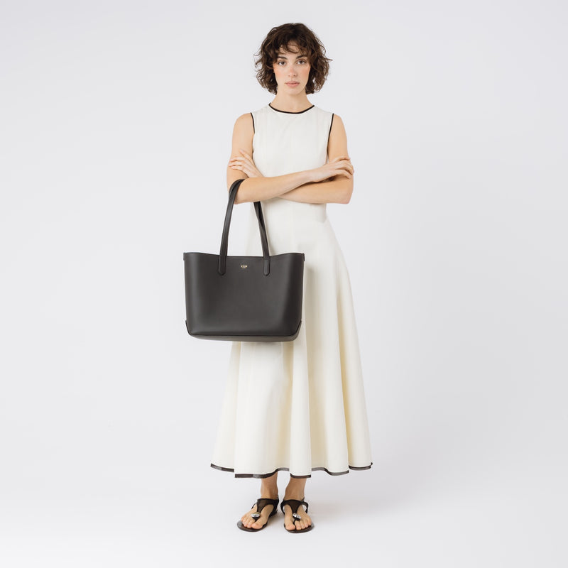 Model wearing Stow London's Everyday Tote Bag in Black smooth leather on her arm on a white background featuring gold STOW logo