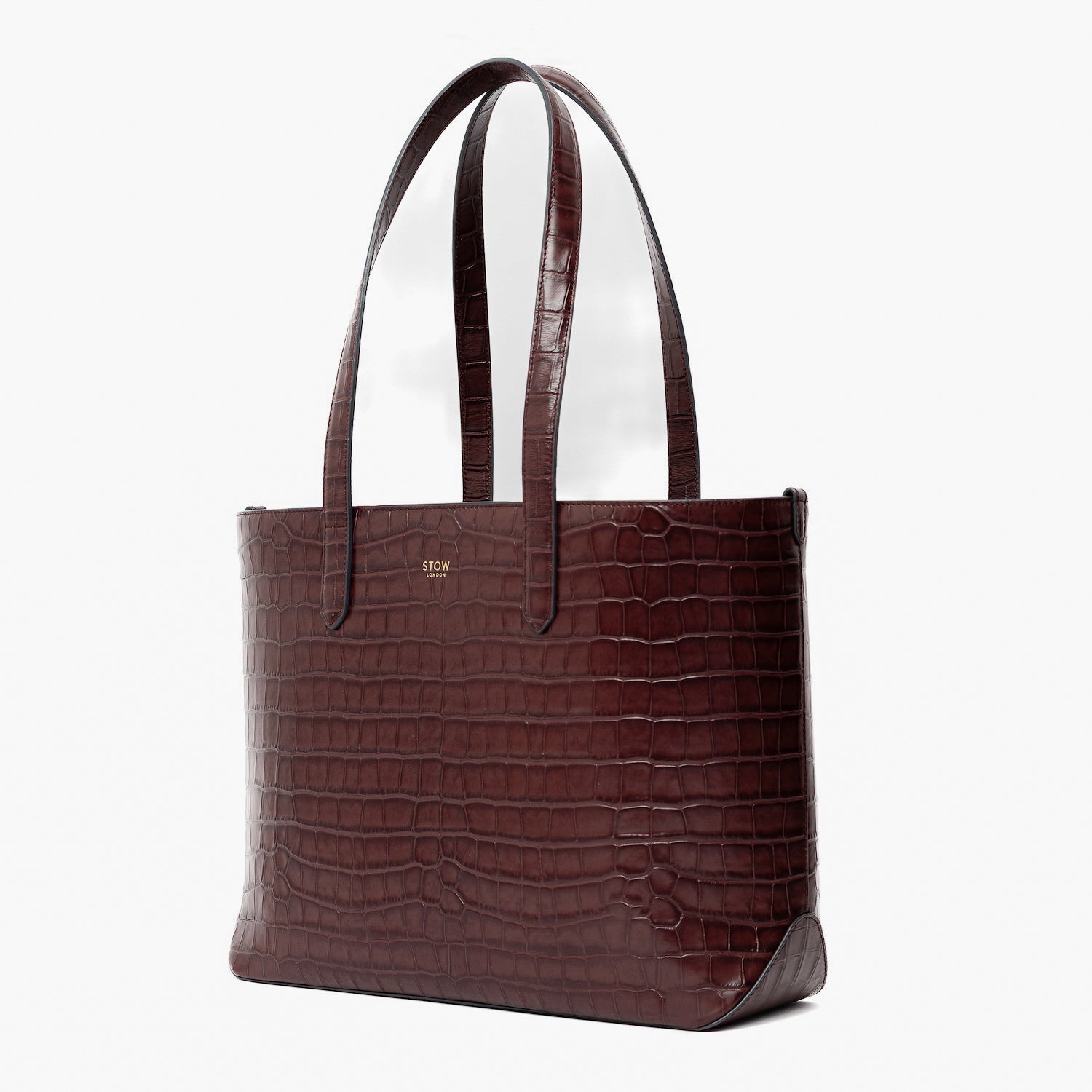 Off-axis view of Stow London's Everyday Tote Bag in Burgundy Embossed Croc leather on a light grey background featuring gold STOW logo