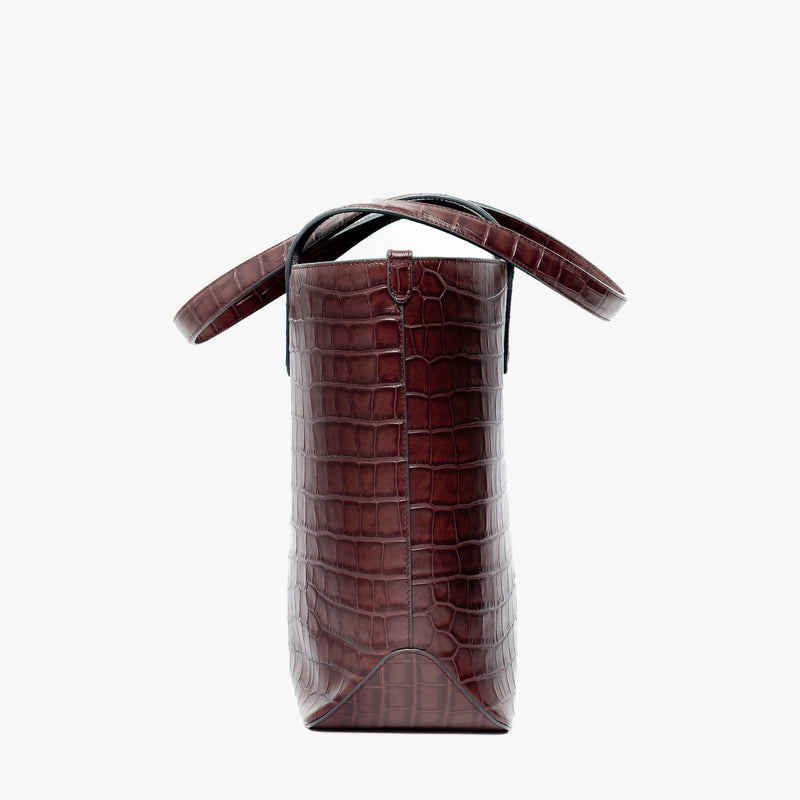 Side view of Stow London's Everyday Tote Bag in Burgundy Embossed Croc leather on a light grey background