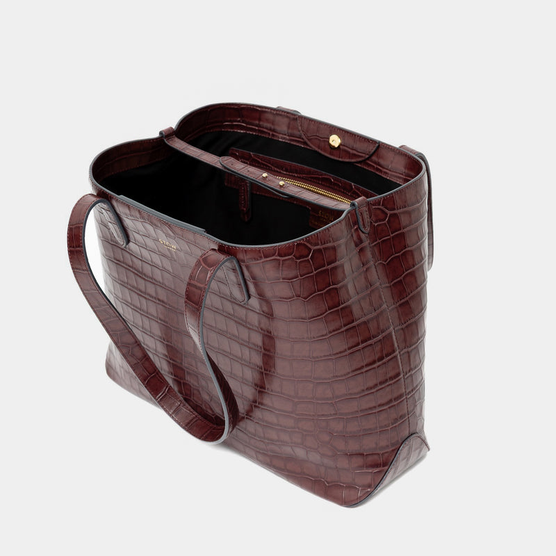 Stow London's Everyday Tote Bag in Burgundy Embossed Croc leather on a light grey background with magnets open showing black cotton interior, leather strap, magnetic closure and zip pocket featuring gold- coated stainless steel hardware