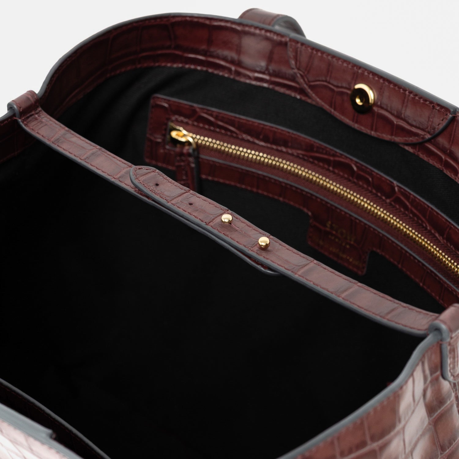 Close up of the leather strap and interior of Stow London's Everyday Tote Bag in Burgundy Embossed Croc leather featuring internal zip pocket and gold-coated stainless steel hardware