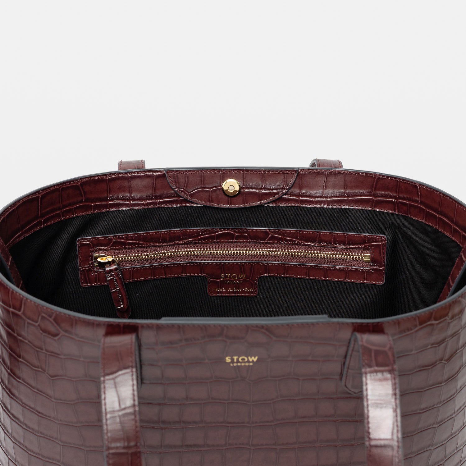 Close up of Stow London's Everyday Tote Bag in Burgundy Embossed Croc leather on a light grey background with magnets open showing black cotton interior and zip pocket