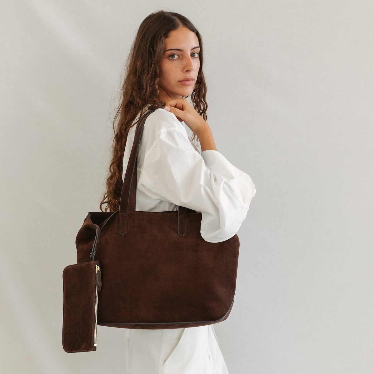 Model wearing STOW London's Everyday Tote bag in Chocolate suede featuring a small STOW London logo embossed on the front panel and the internal matching zip pouch 