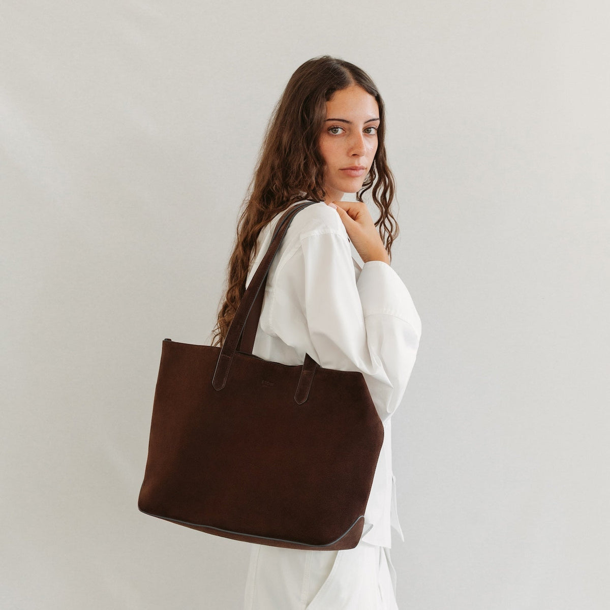 Model wearing STOW London's Everyday Tote bag in Chocolate suede featuring a small STOW London logo embossed on the front panel