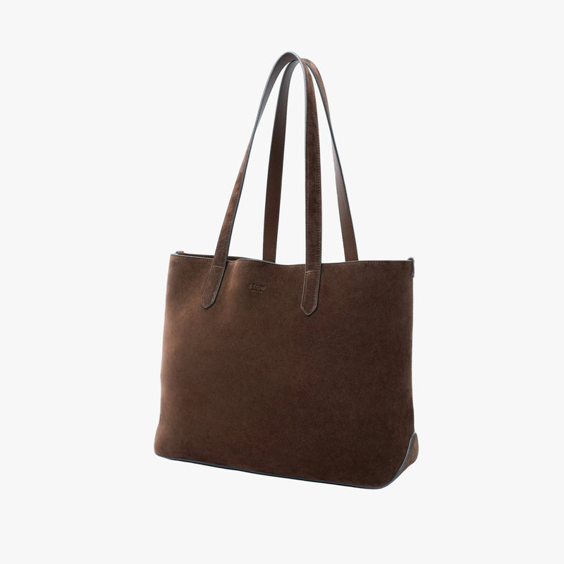 Off-axis view of STOW London's Everyday Tote bag in Chocolate suede on a light grey background featuring a small STOW London logo embossed on the front panel