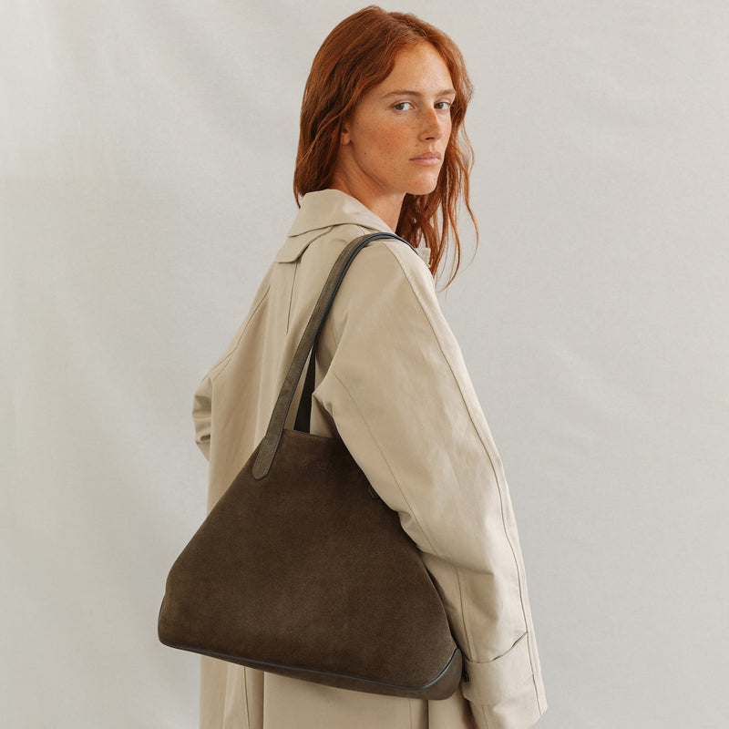 Model wearing STOW London's Everyday Tote bag in Dark Green suede on a light grey background featuring a small STOW London logo embossed on the front panel