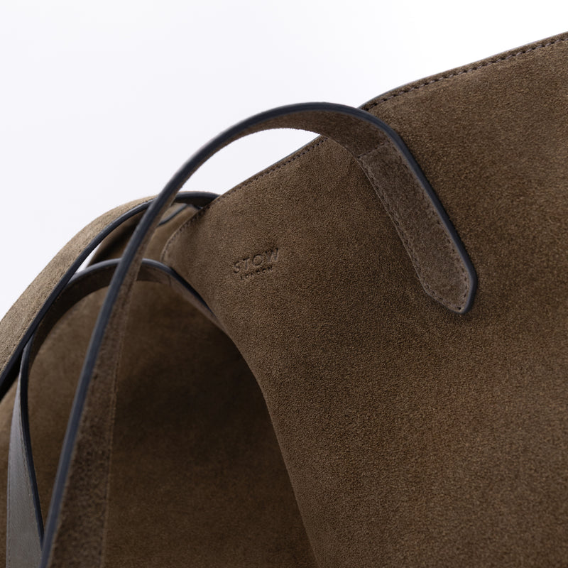 Close up of STOW London's Everyday Tote bag in Dark Green suede on a light grey background featuring a small STOW London logo embossed on the front panel