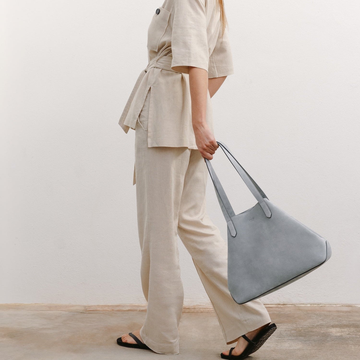 Model with STOW London's Everyday Tote bag in Misty Blue suede featuring a small STOW London logo embossed on the front panel 
