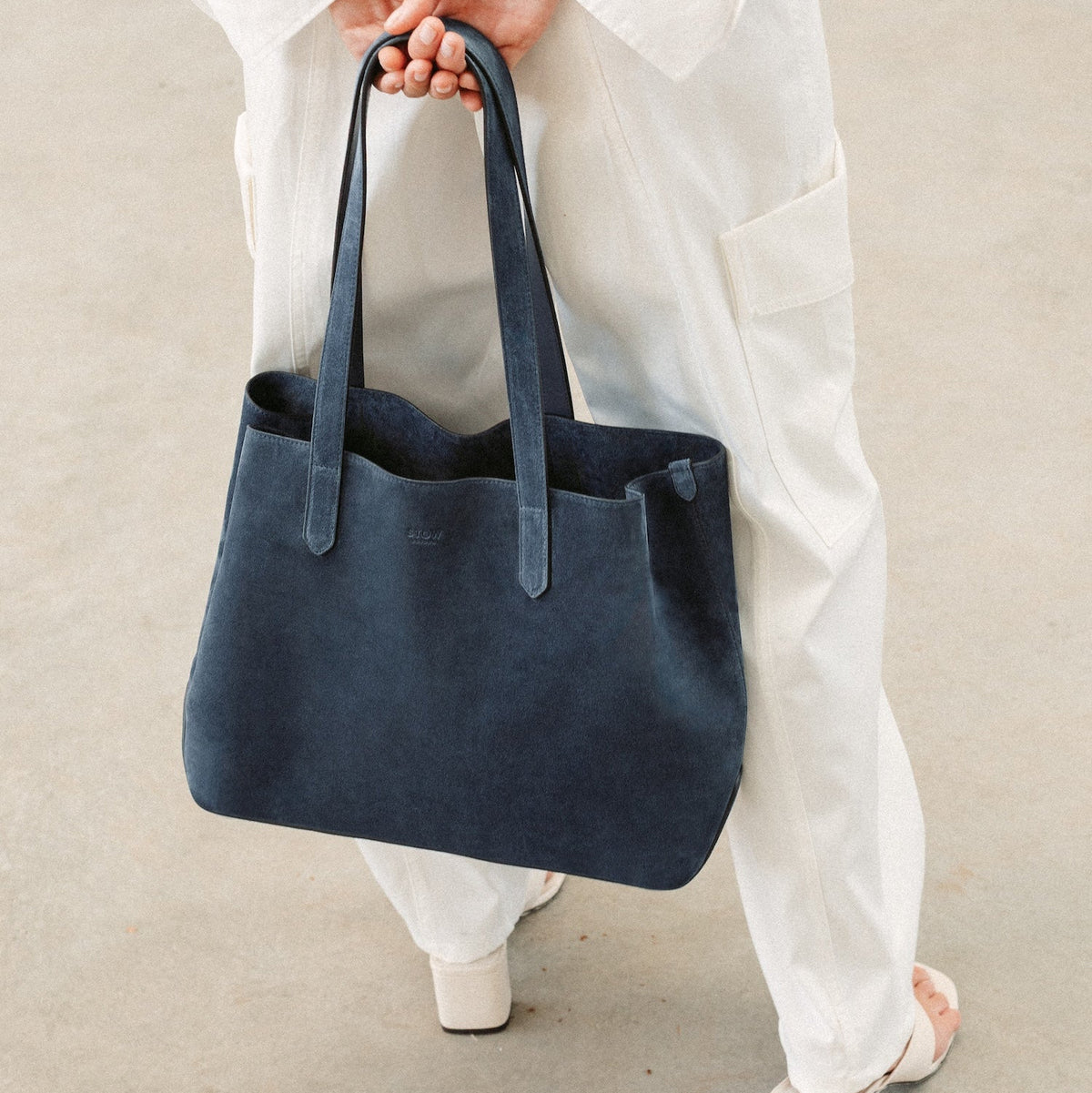 Model wearing STOW London's Everyday Tote bag in Navy suede featuring a small STOW London logo embossed on the front panel
