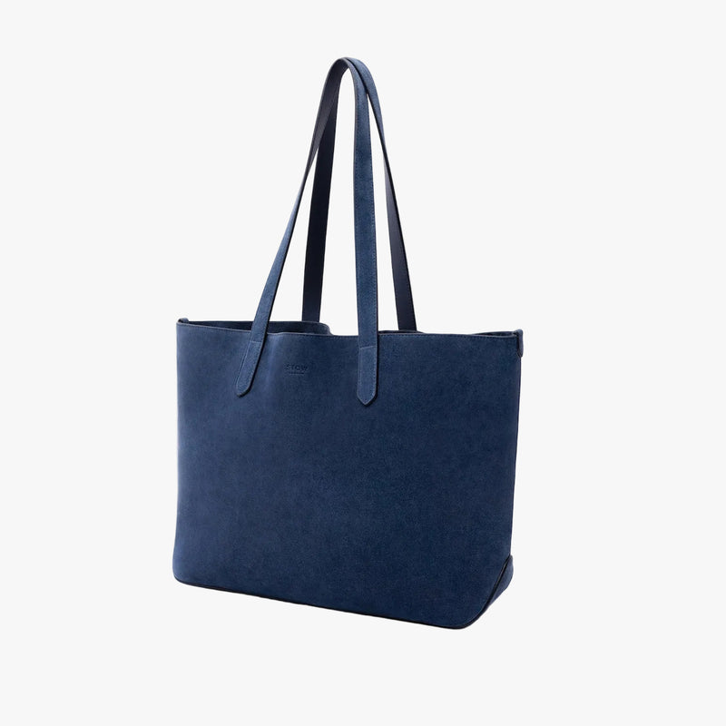 Off-axis view of STOW London's Everyday Tote bag in Navy suede on a light grey background featuring a small STOW London logo embossed on the front panel