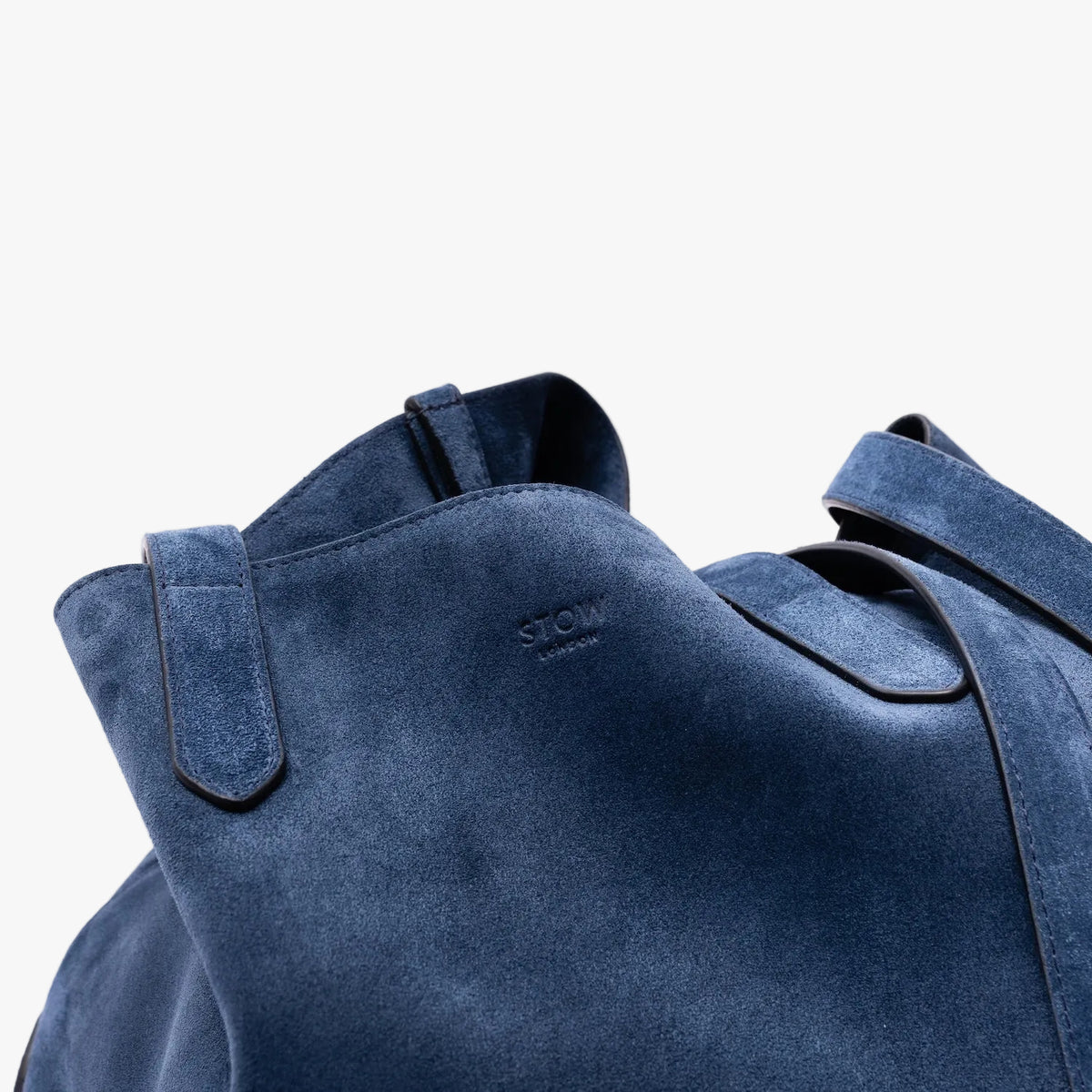 Close-up of a STOW London's Everyday Tote in Navy suede with a small embossed logo, showing the texture and stitching details against a light grey background.