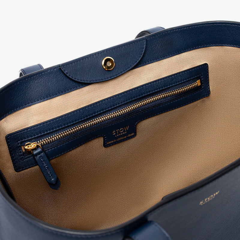 Close up of the interior of Stow London's Everyday Tote Bag in Navy smooth leather on a light grey background featuring the zip pocket, magnetic closure and gold hardware