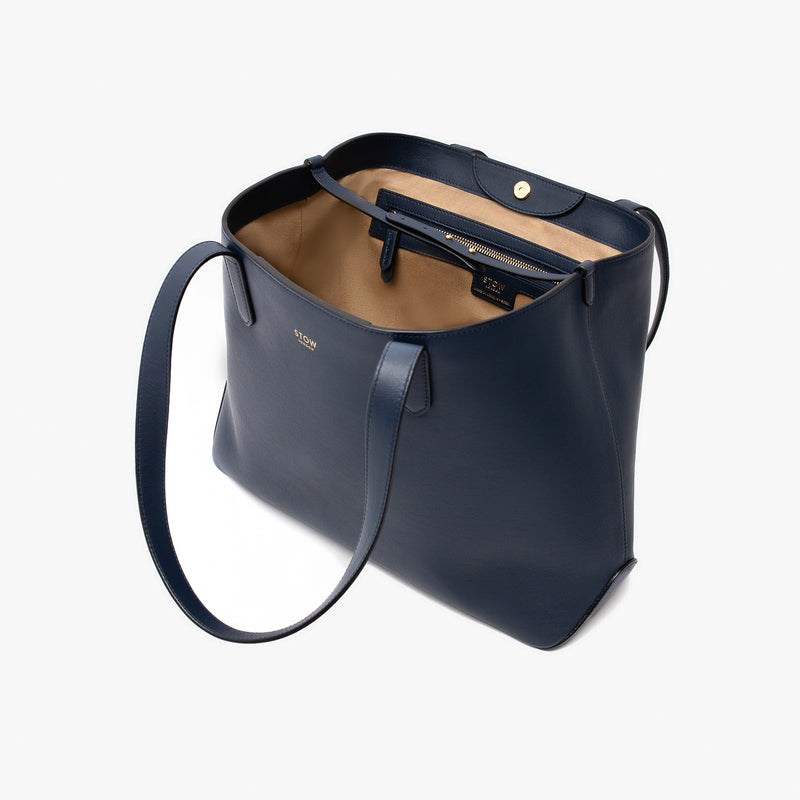 Stow London's Everyday Tote Bag in Navy smooth leather on a light grey background with magnets open showing light beige cotton lining featuring leather strap, magnetic closure and zip pocket